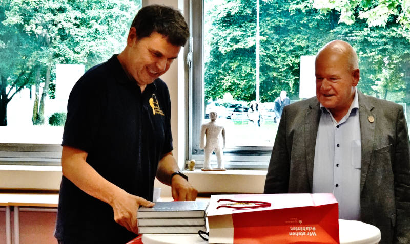 Schulleiter Dr. Maak Flatten und Bürgermeister Peter Ulrich an einem Stehtisch bei der Übergabe von Geschenken.